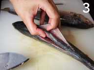 A hand is showing the two slits in a whole fish on a plastic chopping board. A hand is showing the two slits in a whole fish on a plastic chopping board.
