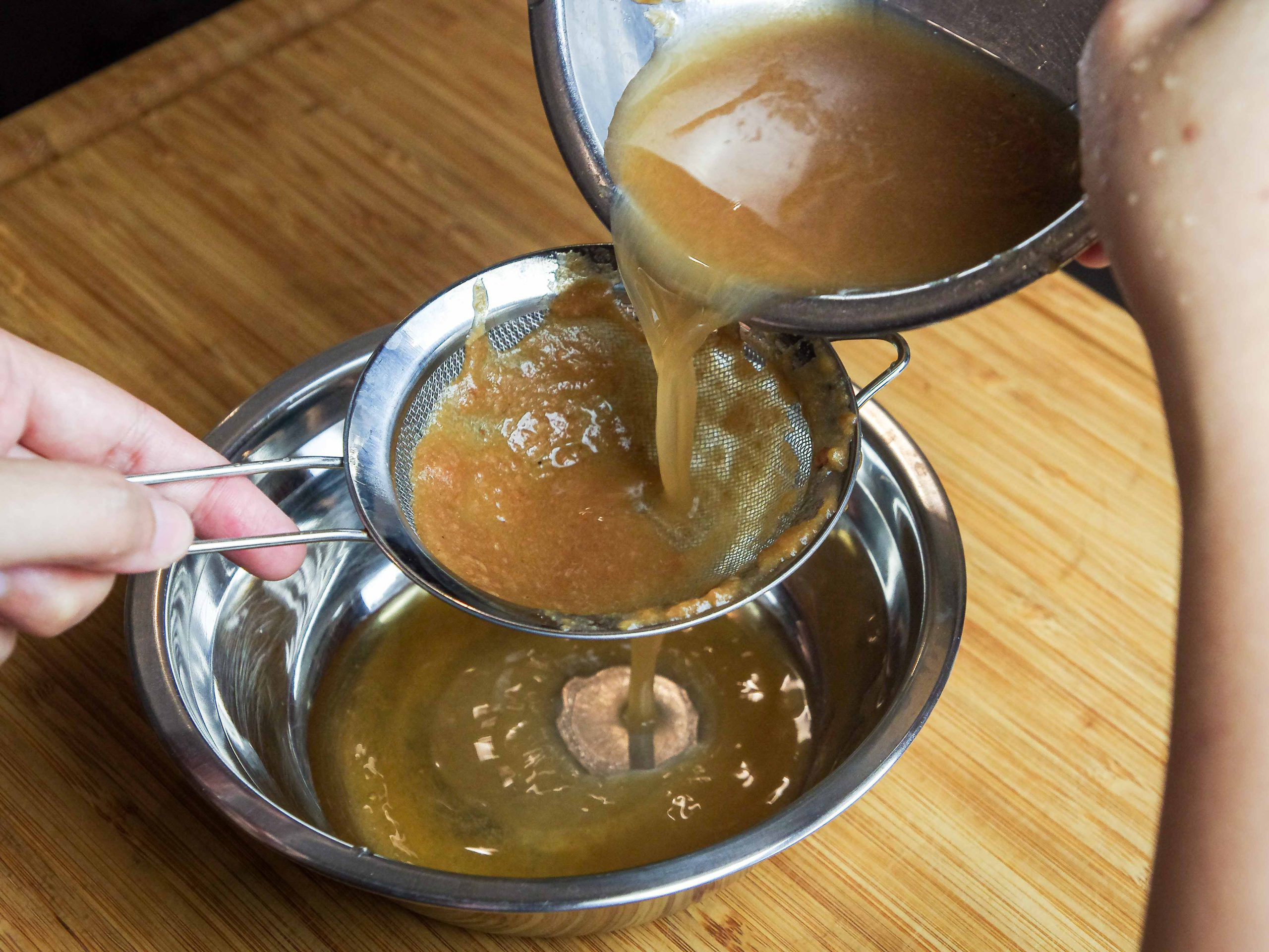 Asam jawa juice being poured into a separate bowl through a strainer.