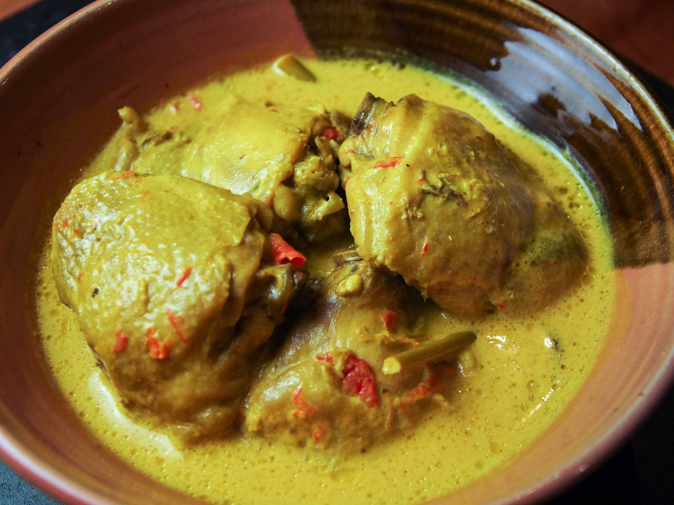 Chicken pieces sit in a yellow gravy, all nestled in a pink-brown bowl on a steel-grey surface.
