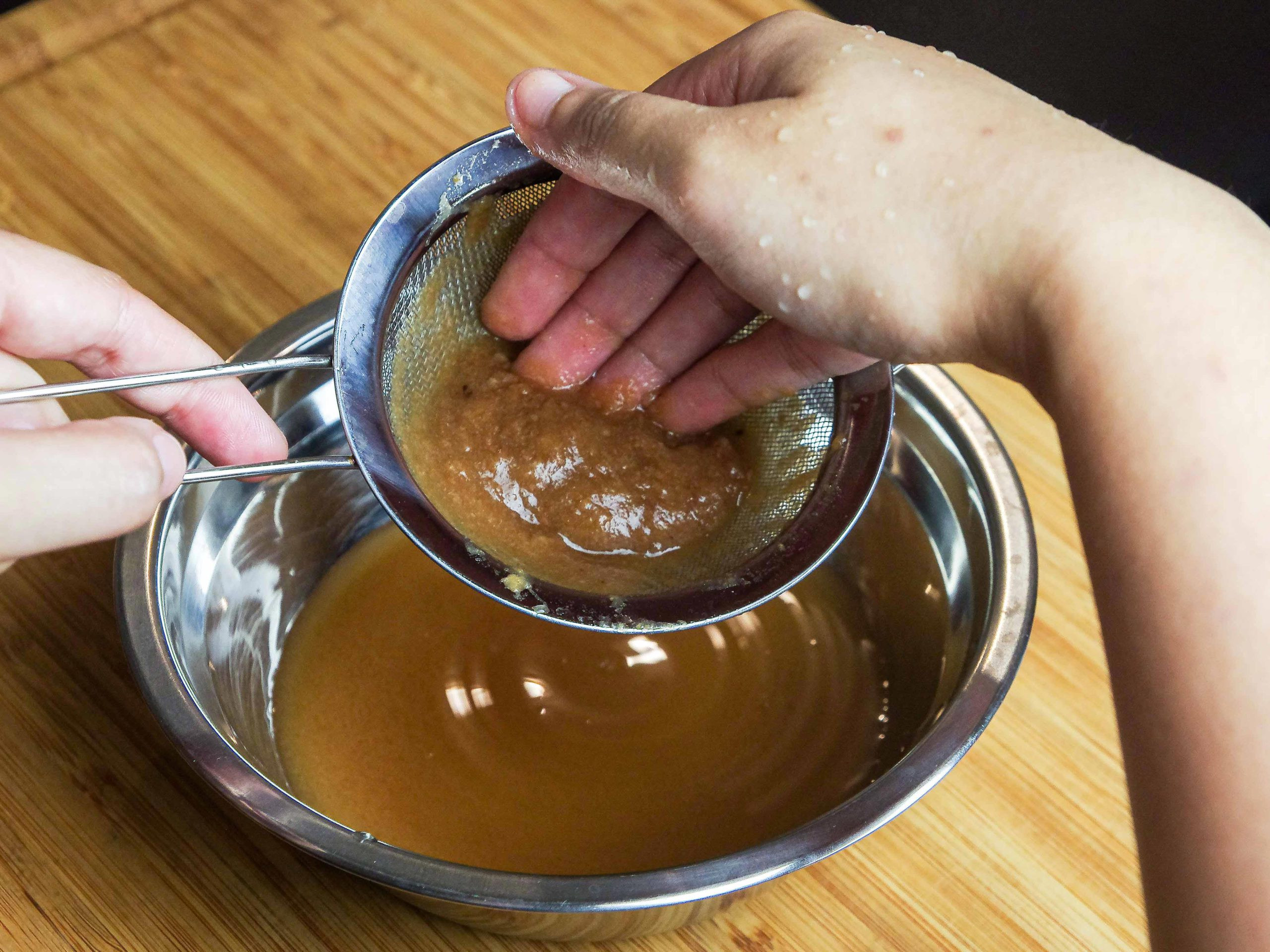 Fingers squeezing pulp on the side of the strainer.