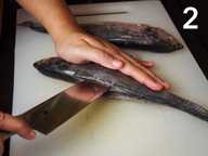 Tangan memegang seluruh ikan di atas papan pencincang plastik. Sebelah tangan lagi memegang pisau dan membuat belahan ke dalam ikan. Tangan memegang seluruh ikan di atas papan pencincang plastik. Sebelah tangan lagi memegang pisau dan membuat belahan ke dalam ikan.
