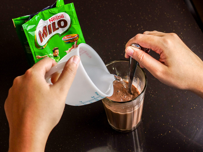 Pouring water into a clear glass, already filled with Milo powder