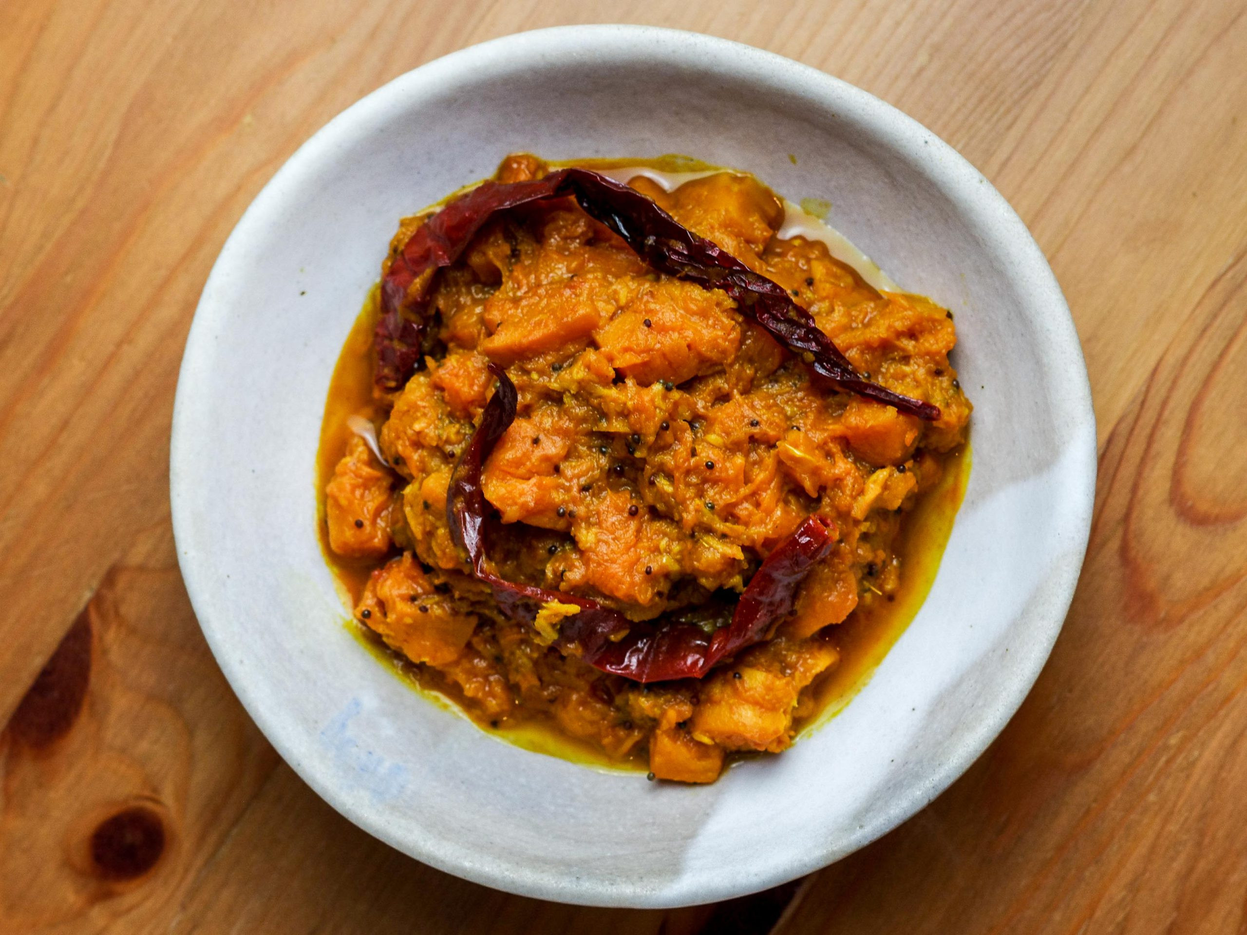 Orange pumpkin masala relaxes in an off-white bowl on a wooden table.